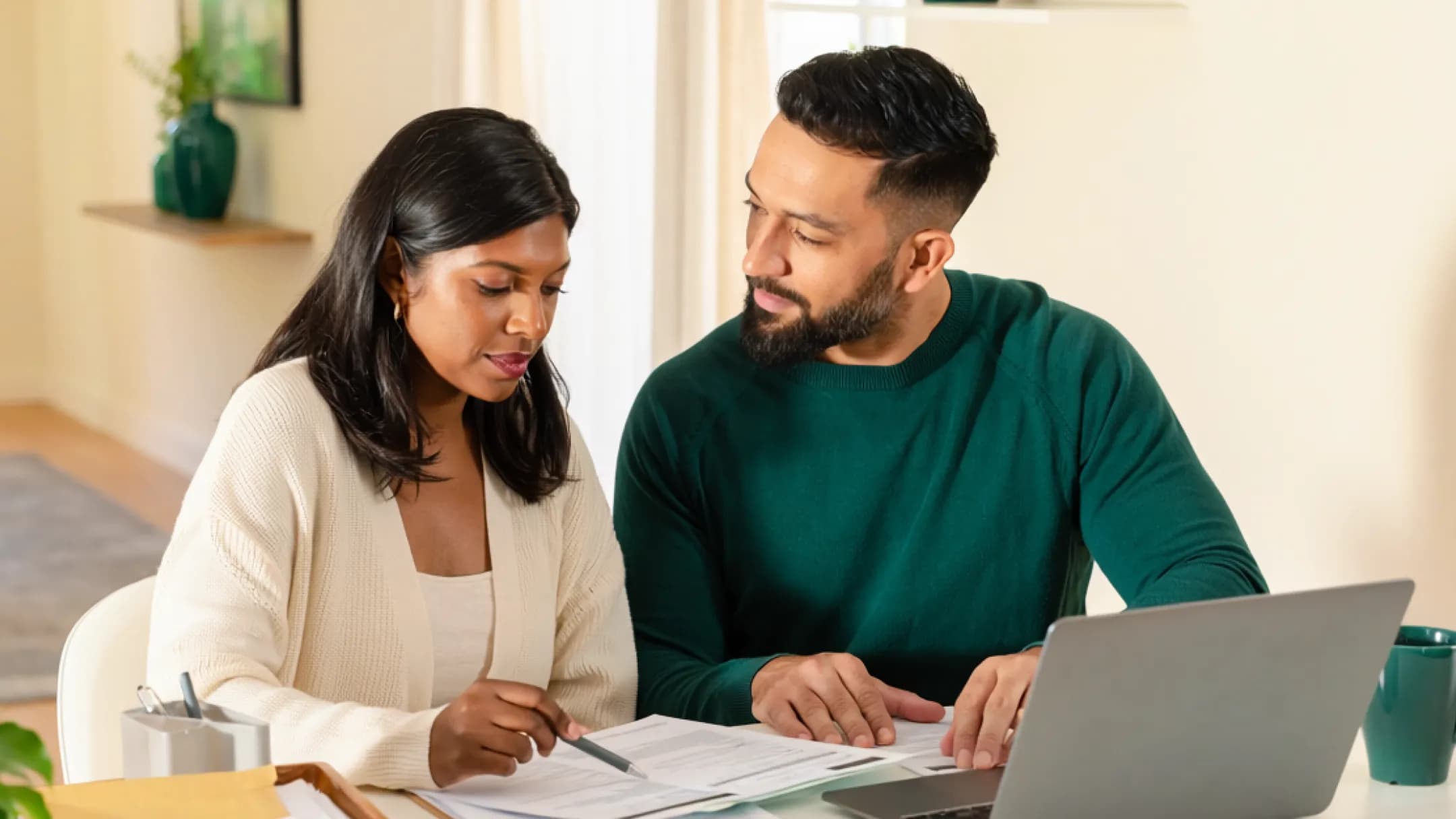 A couple reviewing documents together at a home desk with a laptop