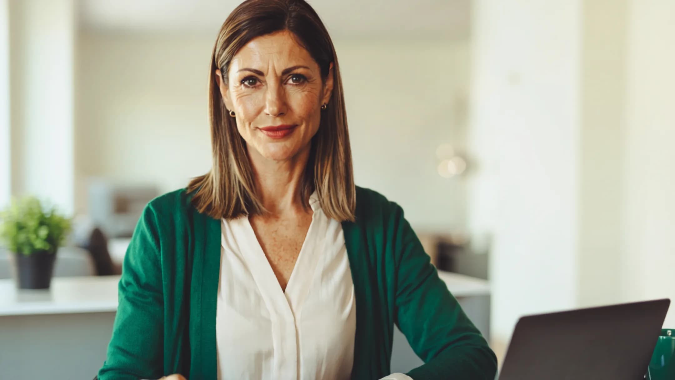 A confident businesswoman in a green cardigan working at her laptop in a bright office