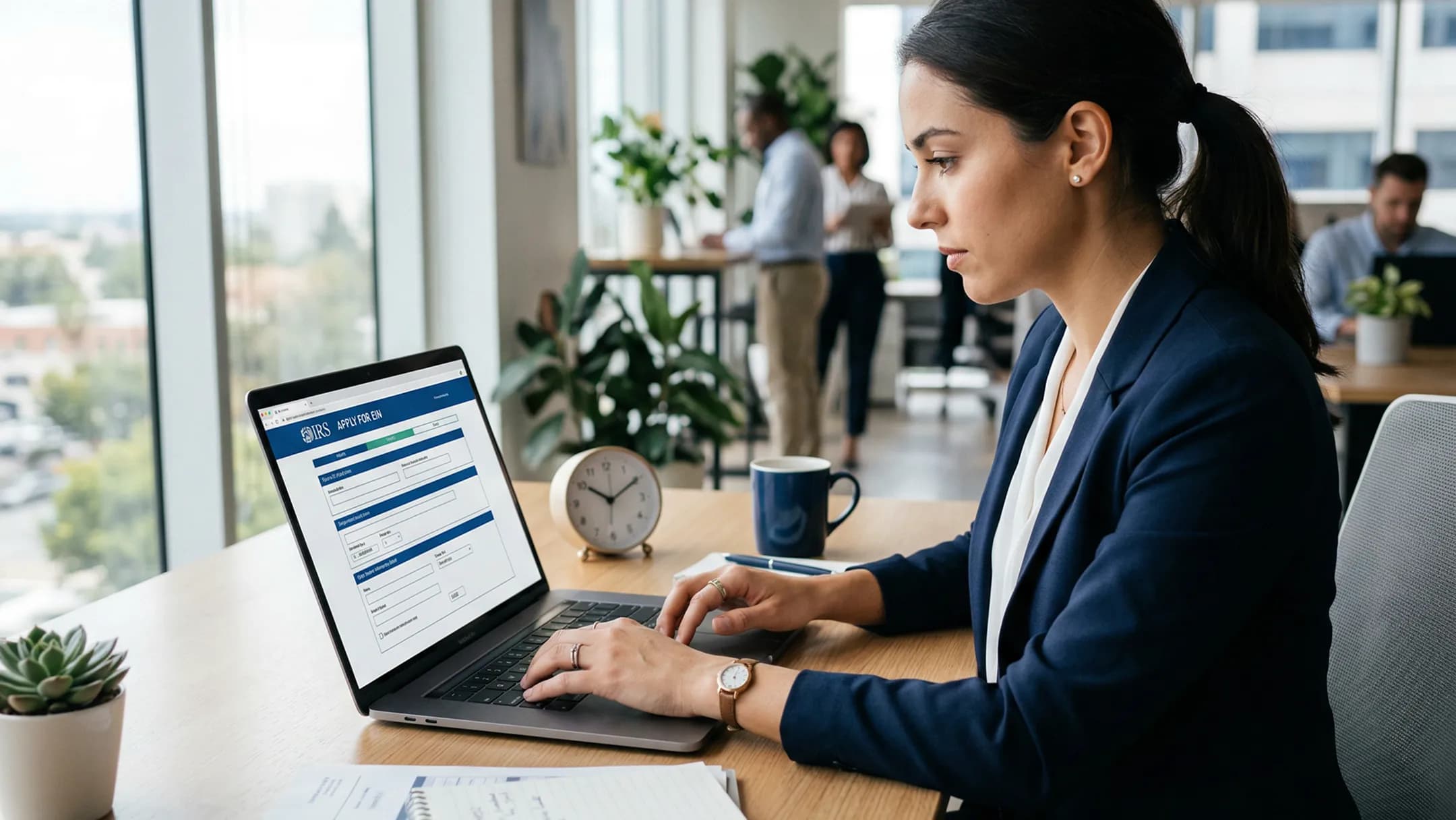 A businesswoman filling out an online application form on a laptop in a busy modern office
